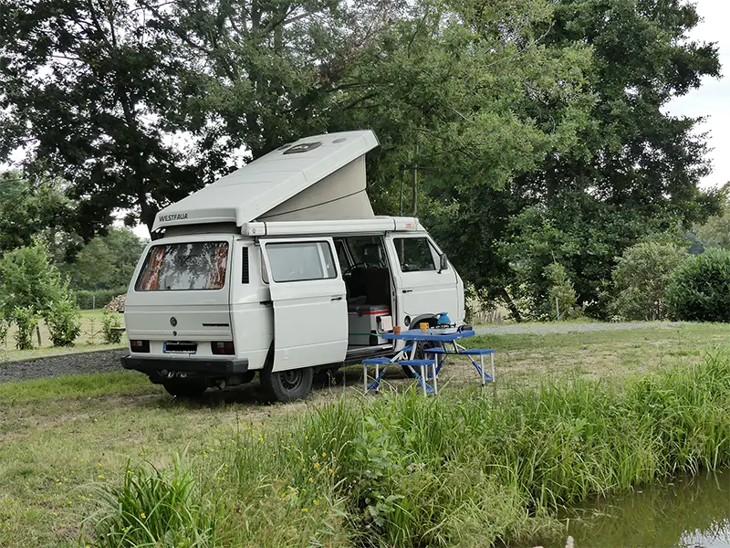 petite-img-tao-6 Image de "Tao" en bivouac au bord d'un lac en pleine nature en Rhône Alpes. La table et les chaises sont sorties. Ce van est en location chez Ryôko - spécialiste de la location de vans pour slow travel dans la Loire.